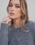 Modèle portant le pull maille oversize gris, stylisé avec de grandes boucles d'oreilles et montrant un look décontracté et moderne.