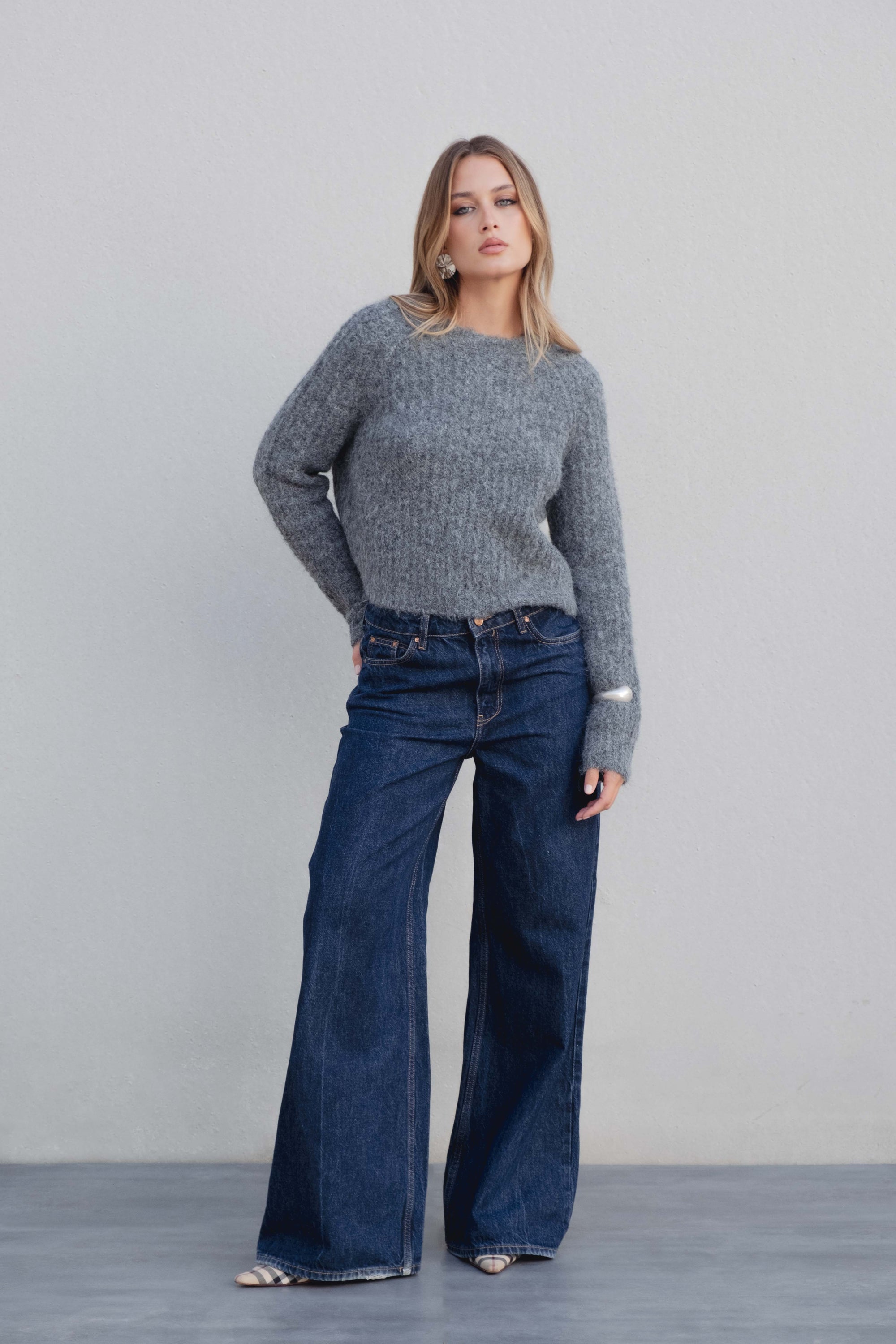 Femme posant avec le pull maille oversize gris, associé à un jean large, dégageant une ambiance décontractée et chic.