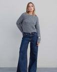 Femme posant avec le pull maille oversize gris, associé à un jean large, dégageant une ambiance décontractée et chic.