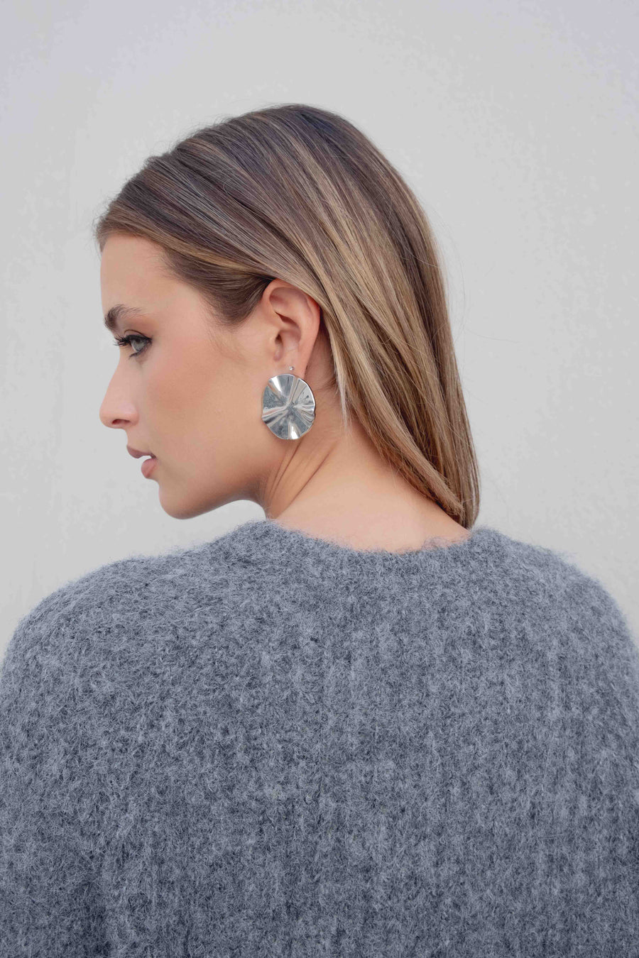 Vue arrière du modèle en pull maille oversize gris, soulignant le design élégant et les boucles d'oreilles stylées.