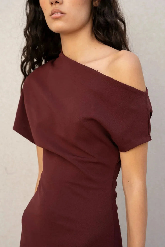 Gros plan sur la robe asymétrique chic bordeaux montrant le détail de la coupe et du tissu, parfaite pour toute occasion.