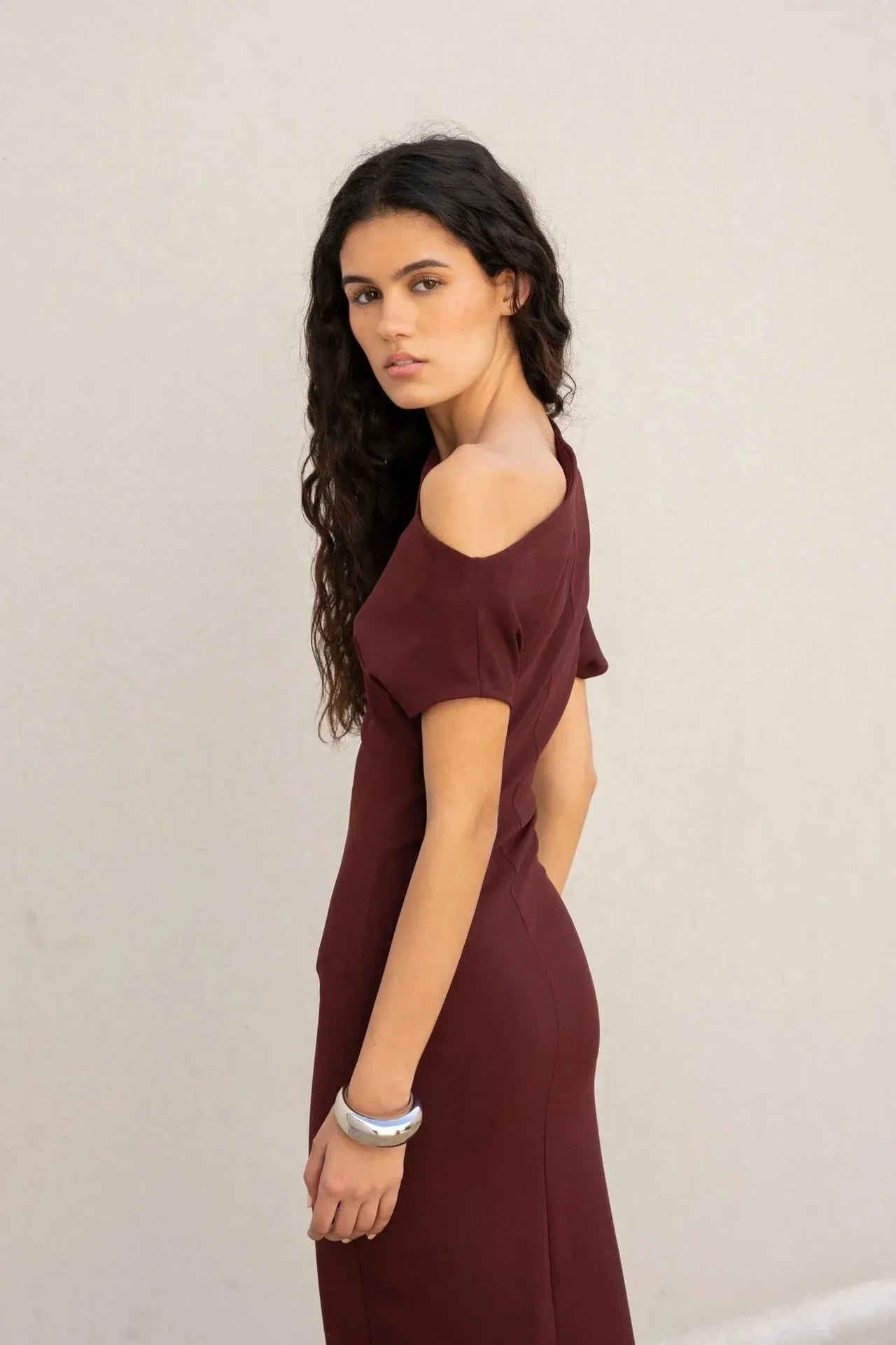 Femme tournant avec une robe asymétrique chic bordeaux – Coupe élégante et polyvalente en polyester, alliant confort et style.