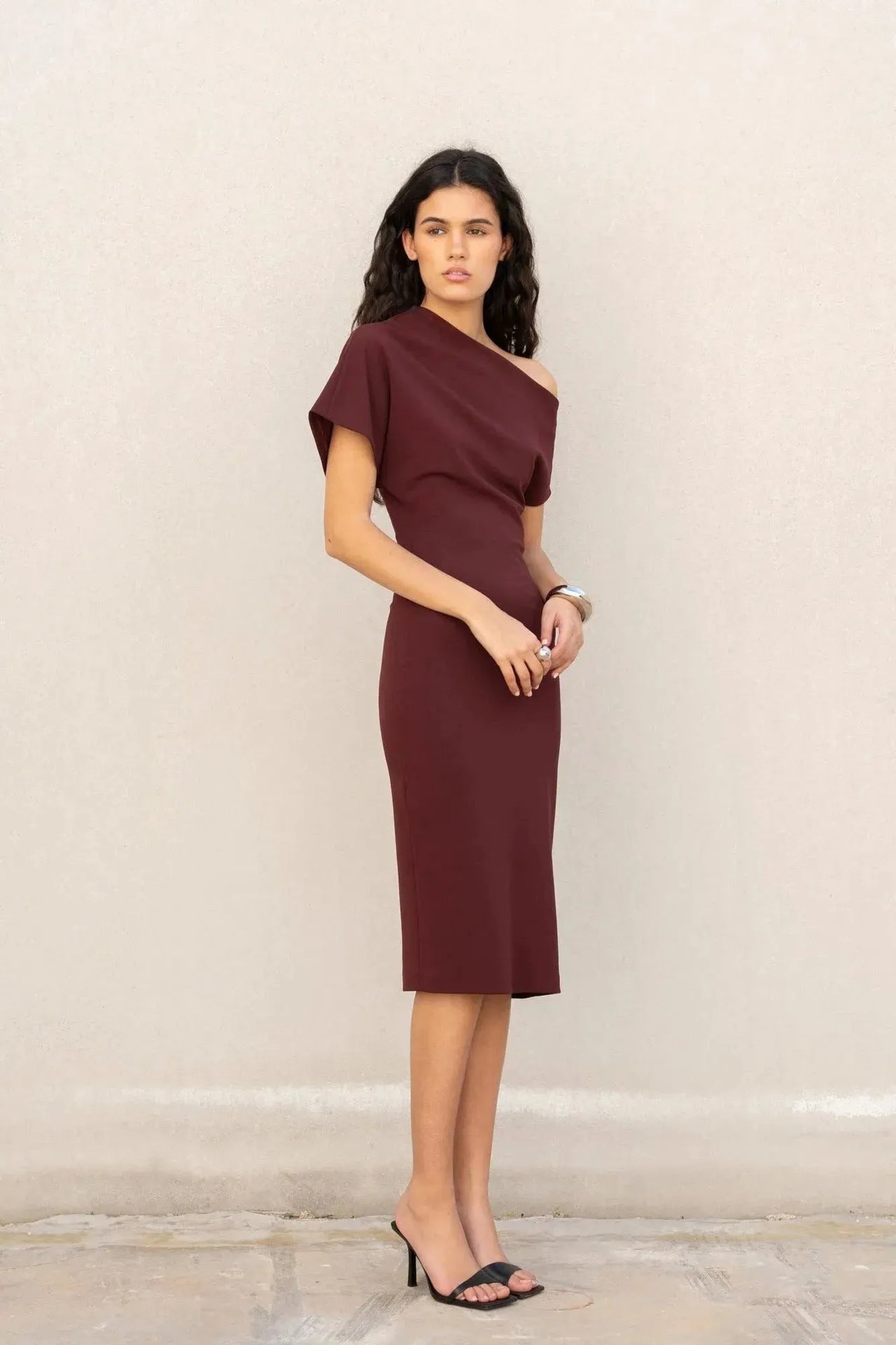 Vue de profil d'une femme en robe asymétrique chic bordeaux – Coupe élégante et polyvalente en polyester, soulignant sa silhouette.