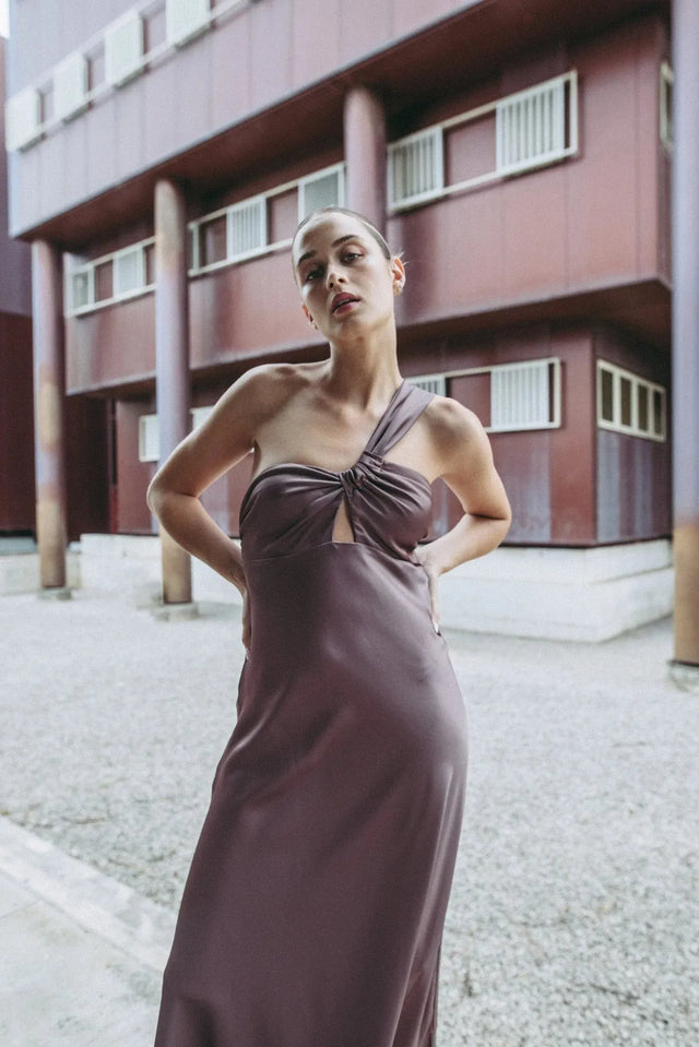 Modèle élégant en robe de soirée femme asymétrique chic en satin marron, mise en scène dans un environnement artistique.