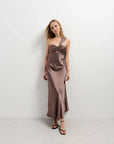 Femme posant fièrement dans une robe de soirée femme asymétrique chic en satin marron, pour un look tendance.