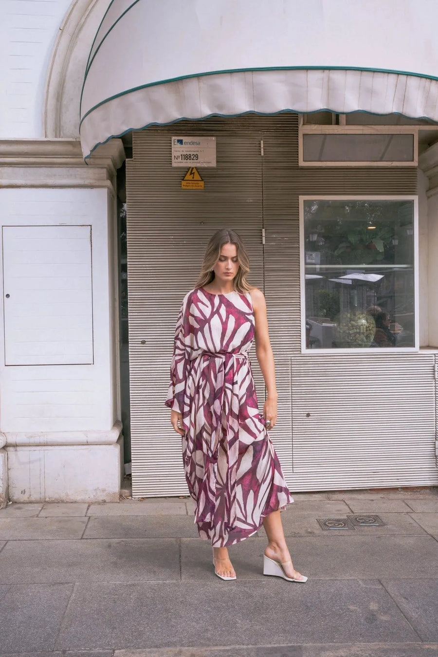 Femme posant contre un fond urbain dans une robe asymétrique imprimée, incarnant l'esprit de la robe hippie année 70.