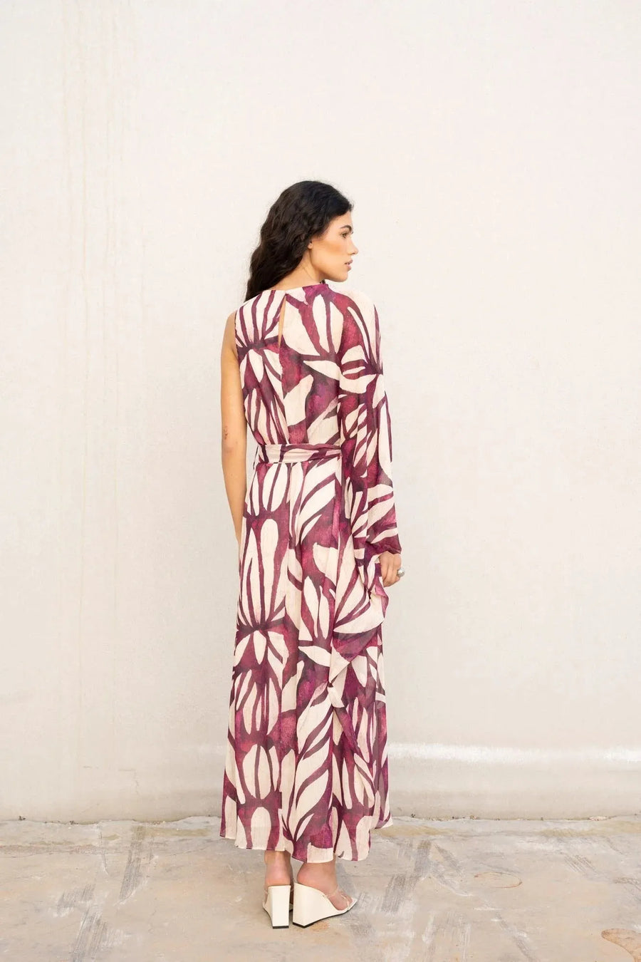 Vue arrière d'une femme prête à sortir dans une robe asymétrique imprimée, inspirée de la robe hippie année 70, arborant des motifs vibrants.