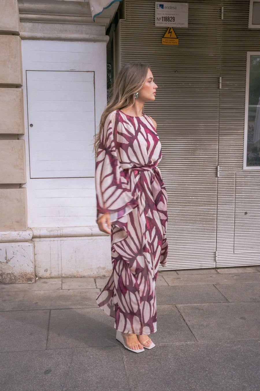 Femme marchant dans la rue avec une robe asymétrique imprimée, rappelant le style robe hippie année 70, avec des détails stylistiques.