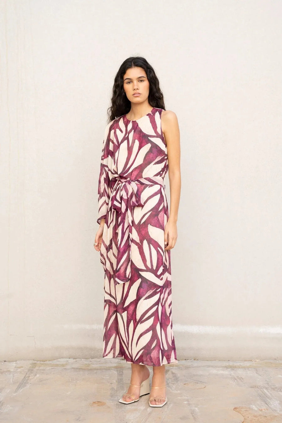 Modèle debout en robe asymétrique imprimée, ceinturée, reflétant le style de la robe hippie année 70, parfaite pour l'été.