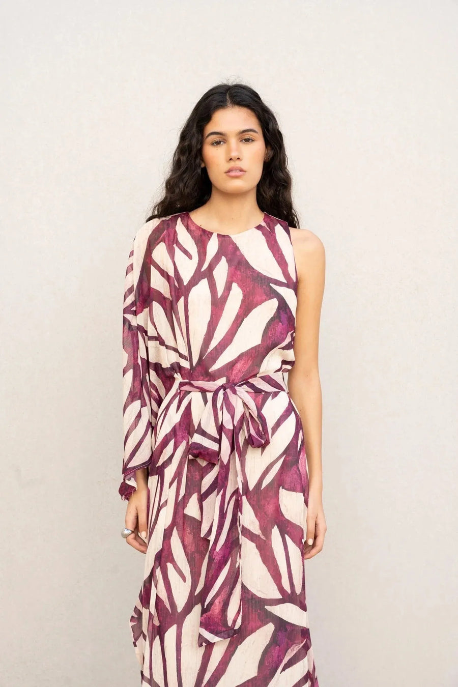 Femme debout dans une robe asymétrique imprimée, rappelant le style robe hippie année 70, avec une ceinture mettant en avant sa silhouette.
