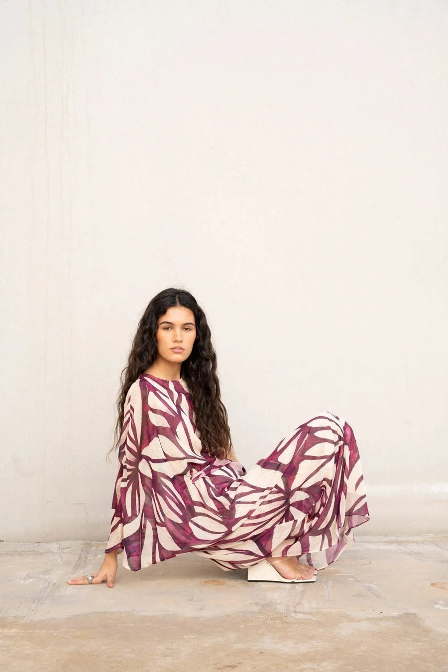 Femme posant avec élégance dans une robe asymétrique imprimée chic, inspirée de la robe hippie année 70, avec des motifs artistiques bordeaux.