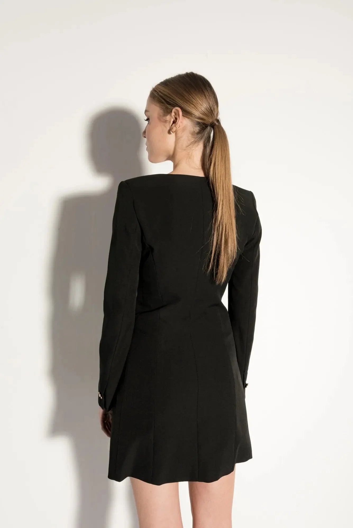 Femme en robe blazer noire élégante avec décolleté en V et jupe évasée, style structuré