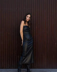 Femme stylée en robe longue simili cuir noir bustier midi avec fente latérale - Élégance Audacieuse, avec des bottes pour un look tendance.