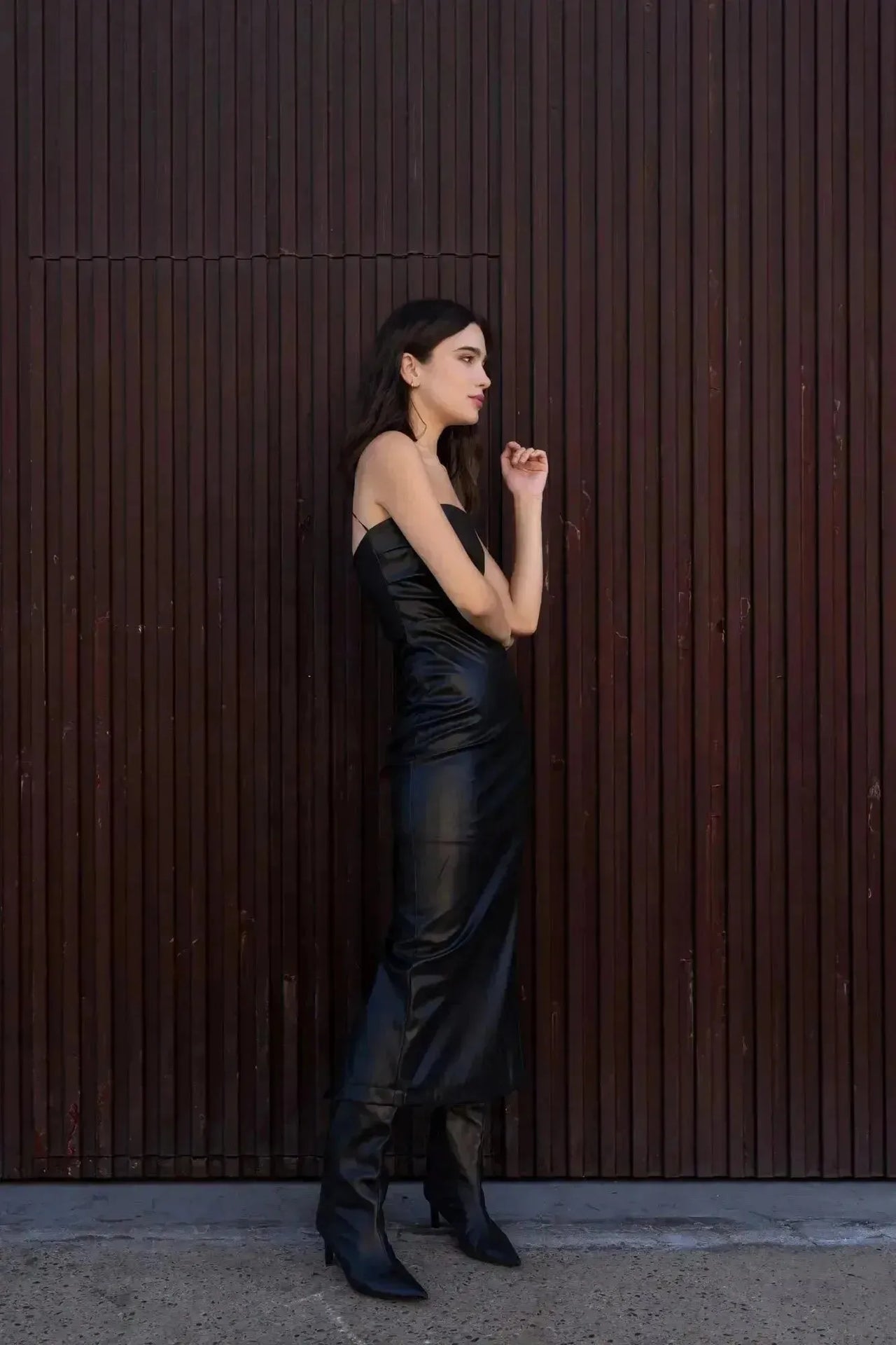 Femme en robe longue simili cuir noir bustier midi avec fente latérale - Élégance Audacieuse, dans une pose contemporaine.