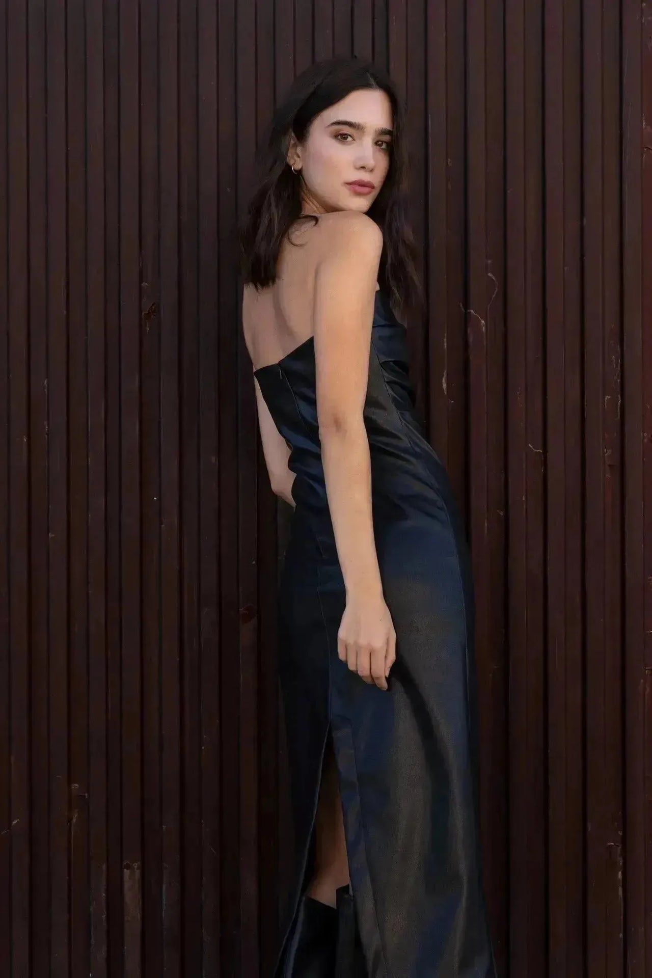 Vue latérale d'un modèle dans une robe longue simili cuir noir bustier midi avec fente latérale - Élégance Audacieuse, mettant en avant la coupe flatteuse.