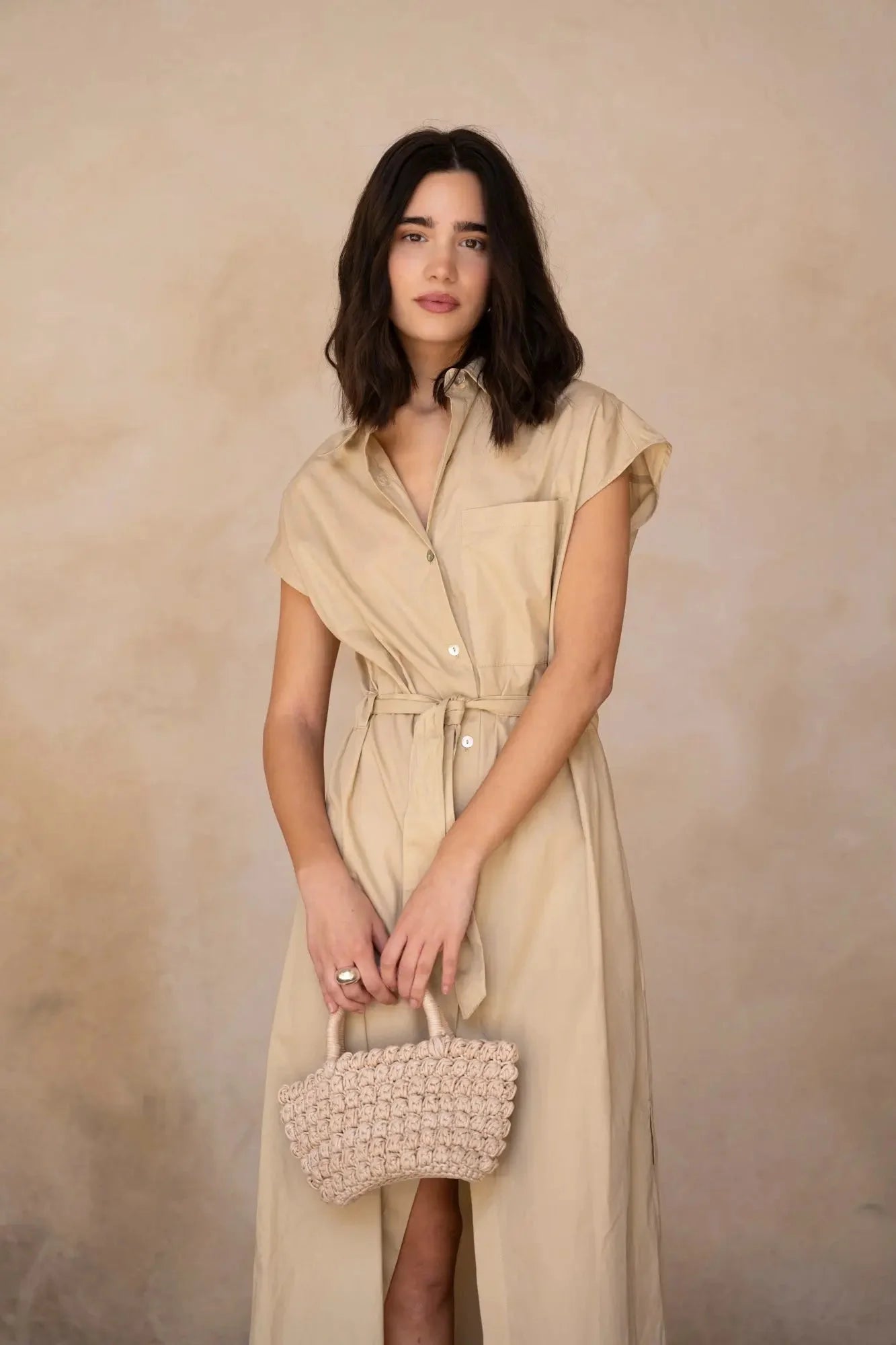Modèle portant une robe chemise femme beige midi ceinturée, mettant en valeur son élégance fluide en popeline, avec un sac en paille.