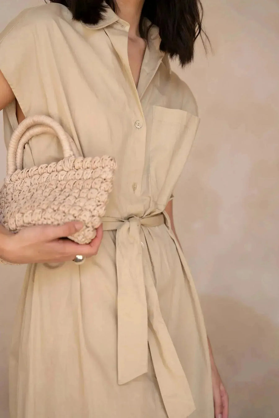 Zoom sur la robe chemise femme beige midi ceinturée, mettant en avant le détail de la ceinture et le sac en paille, parfaite pour un look estival.