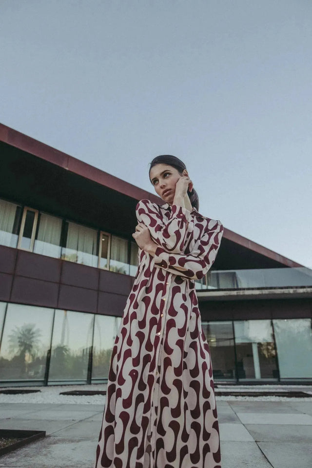 Femme en robe chemise longue imprimée bordeaux devant un bâtiment moderne, montrant le style chic de la pièce.