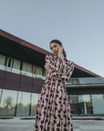 Femme en robe chemise longue imprimée bordeaux devant un bâtiment moderne, montrant le style chic de la pièce.