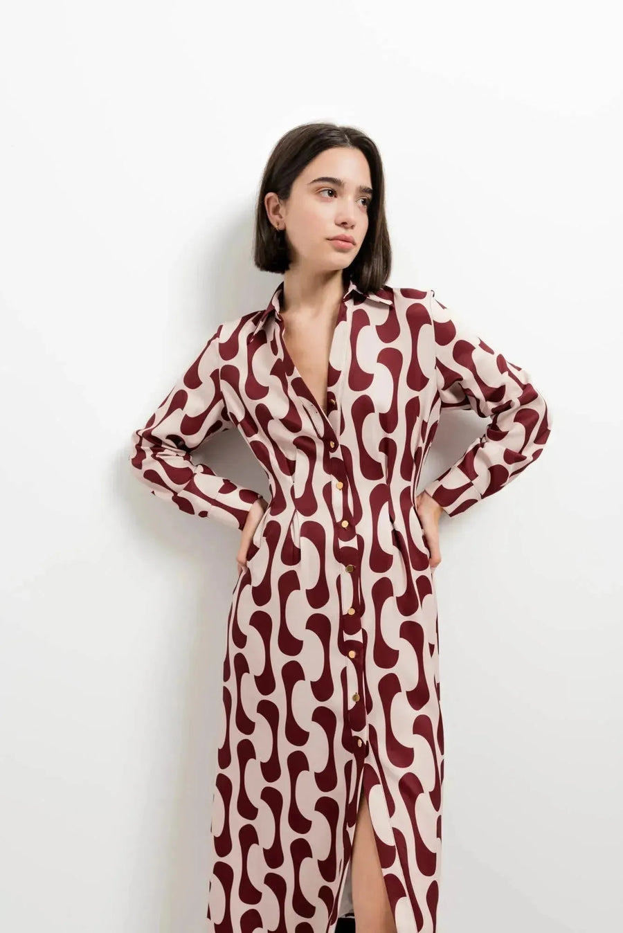 Portrait d'une femme en robe chemise longue imprimée bordeaux, stylée avec des boutons dorés et un col chemise, avec une expression calme.