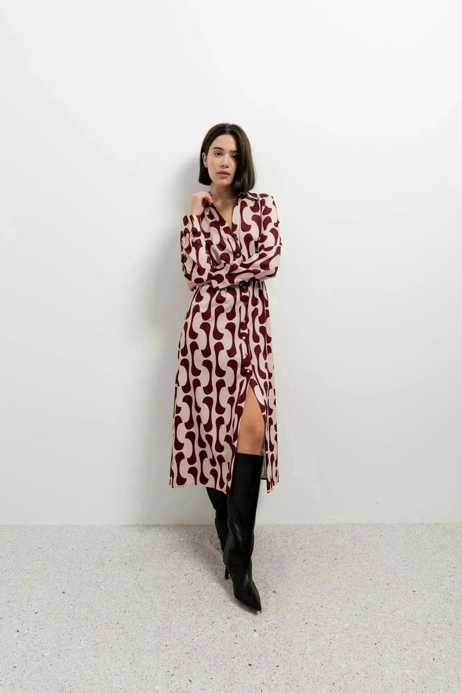 Femme en robe chemise longue imprimée bordeaux avec une coupe fluide, ajoutant une ceinture pour structurer sa silhouette.