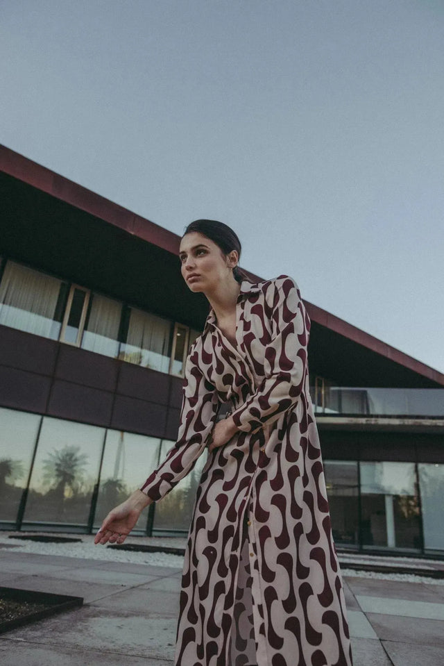 Femme en robe chemise longue imprimée bordeaux, prenant une pose dynamique à l'extérieur, mettant en valeur le design moderne et élégant.