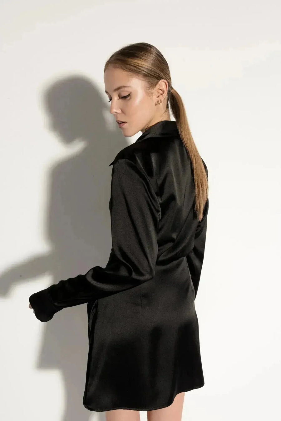 Robe chemise satin noir courte – Élégante et chic avec effet portefeuille croisé, vue arrière sur un mannequin, mettant en valeur le design fluide et féminin.