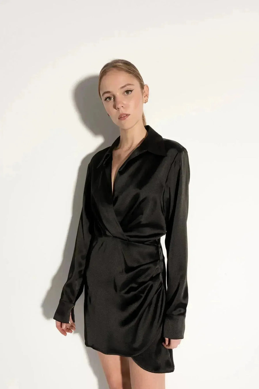 Robe chemise satin noir courte – Élégante et chic avec effet portefeuille croisé, portée par un mannequin, montrant le col chemise classique et les manches longues.