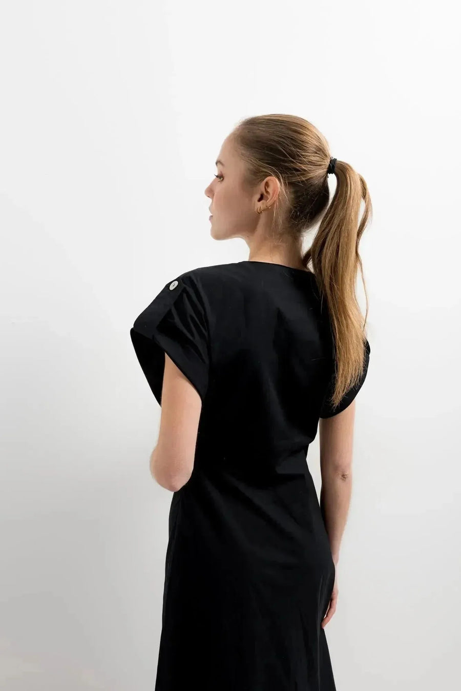 Vue arrière d'une femme portant une robe popeline noire chic à manches courtes - décolleté en V évasée pour toutes occasions, sur fond blanc.