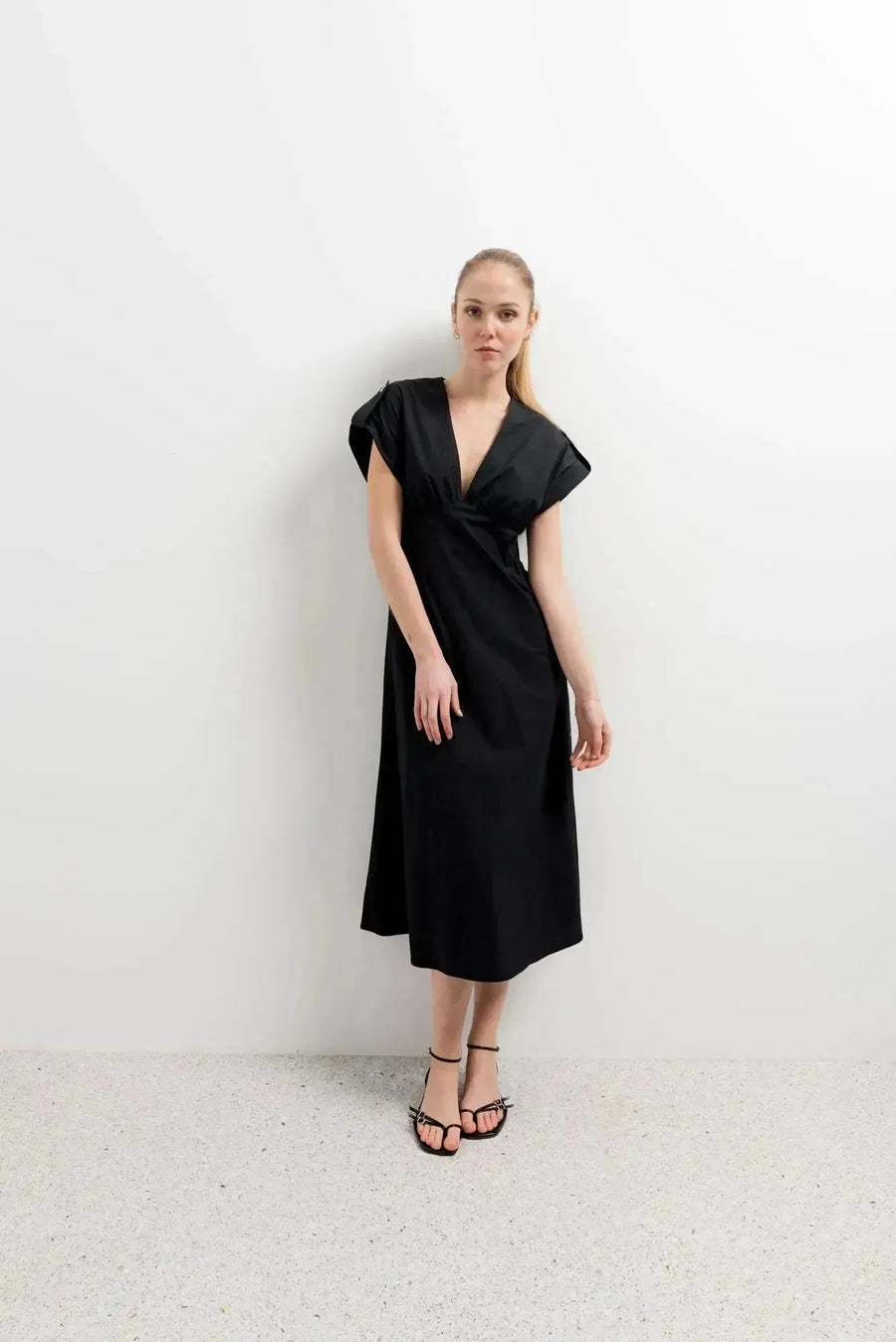 Femme posant avec une robe popeline noire chic à manches courtes - décolleté en V évasée pour toutes occasions, devant un mur contemporain.