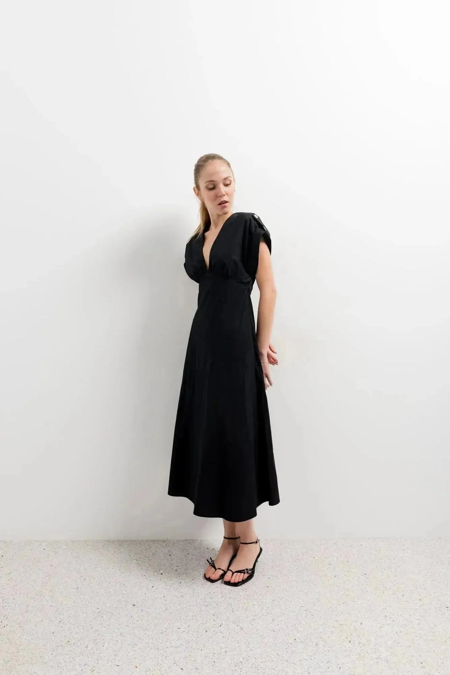 Modèle mettant en valeur une robe popeline noire chic à manches courtes - décolleté en V évasée pour toutes occasions, sur fond blanc.
