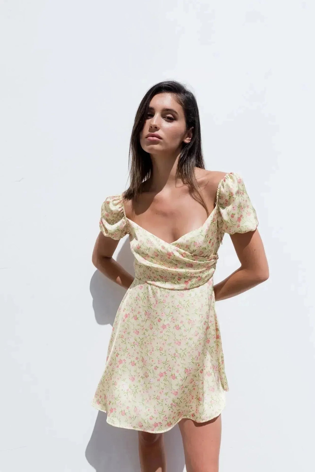 Vue rapprochée d'un modèle en Mini Robe Florale Romantique Jaune Pâle Avec Décolleté Cache-Cœur Et Manches Bouffantes, affichant une expression confiante.