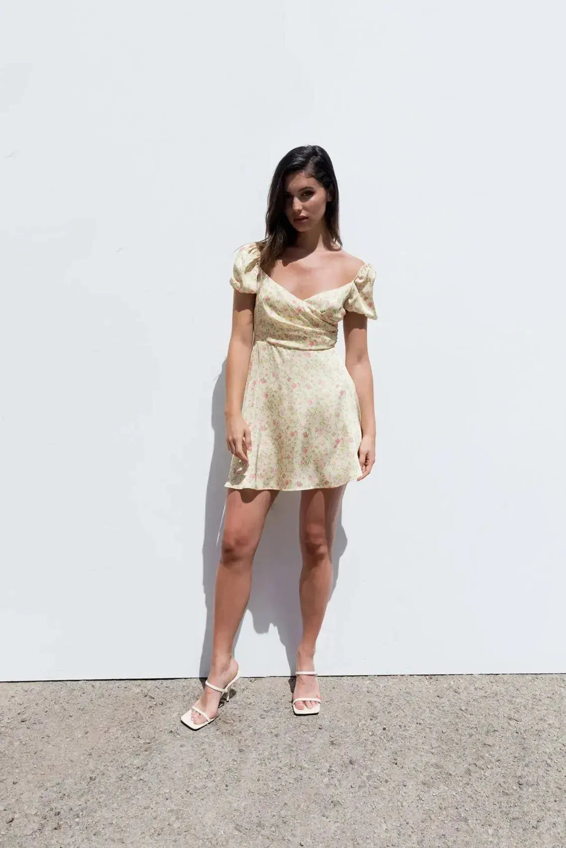 Modèle portant une Mini Robe Florale Romantique Jaune Pâle Avec Décolleté Cache-Cœur Et Manches Bouffantes, se tenant devant un fond blanc.