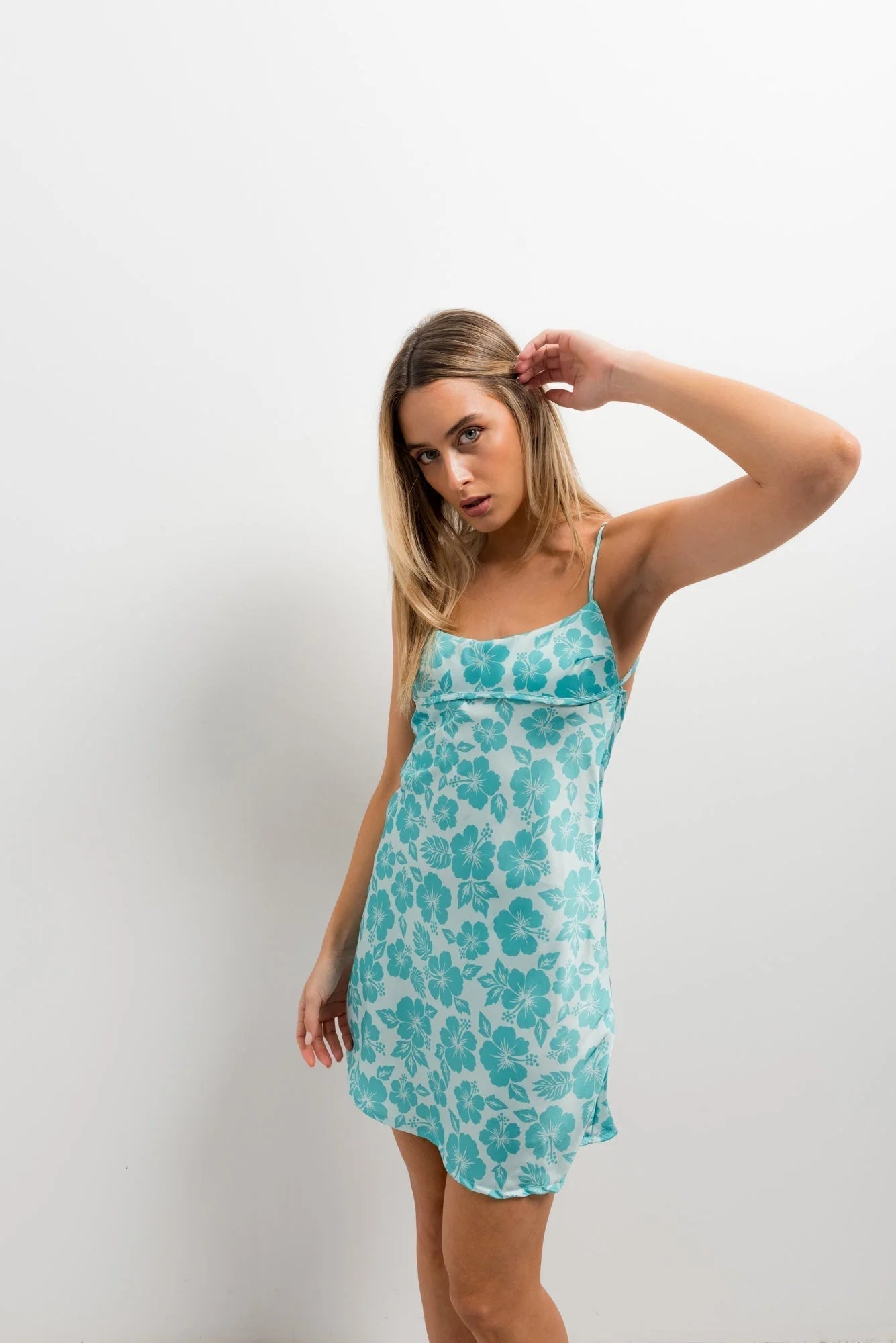 Femme en robe courte satinée turquoise à fleurs avec spaghetti straps