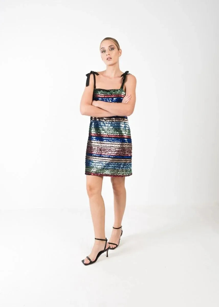 Modèle portant une robe courte à paillettes multicolores, élégante et chic pour soirées festives, mise en valeur par des bretelles noires à nouer.