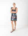 Modèle portant une robe courte à paillettes multicolores, élégante et chic pour soirées festives, mise en valeur par des bretelles noires à nouer.