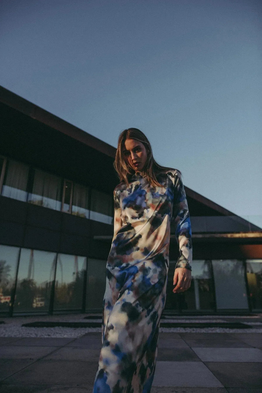Femme portant une robe satin longue manche longue imprimée aquarelle, se tenant devant un bâtiment moderne, mettant en évidence l'élégance artistique et chic de la robe.