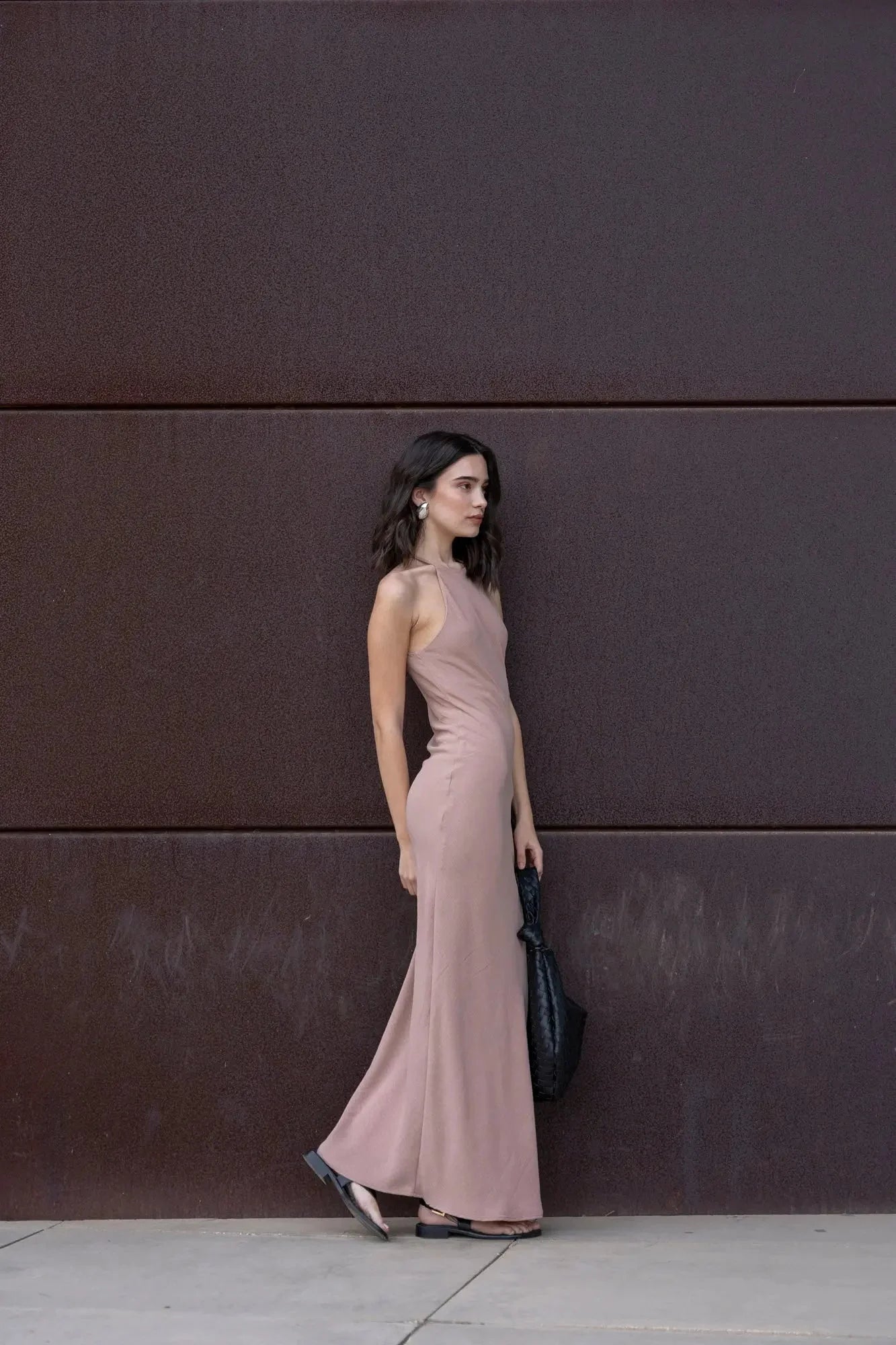 Femme portant une robe halter élégante mauve longue, sac noir et sandales plates