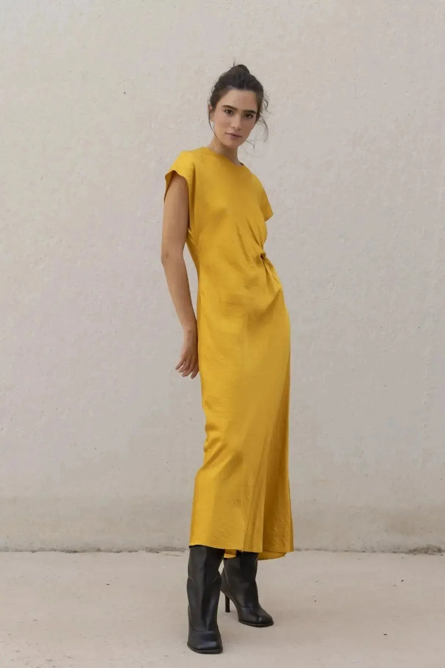 Robe De Soirée Jaune Satinée Élégante Avec Nœud À La Taille - Chic Et Fluide, modèle féminin posant en robe de soirée jaune avec des bottes noires.