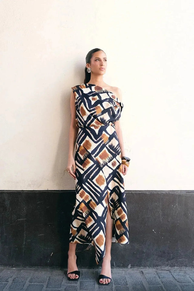 Une femme en haut femme asymétrique à une épaule imprimé graphique marron, noir et blanc, posant contre un mur. Ce style chic et moderne est parfait pour diverses occasions.