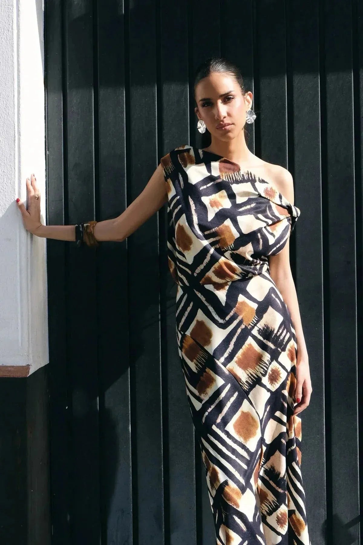 Haut femme asymétrique à une épaule imprimé graphique marron, noir et blanc, porté par une femme élégante devant une porte. Chic et moderne, ce vêtement met en valeur le style unique.