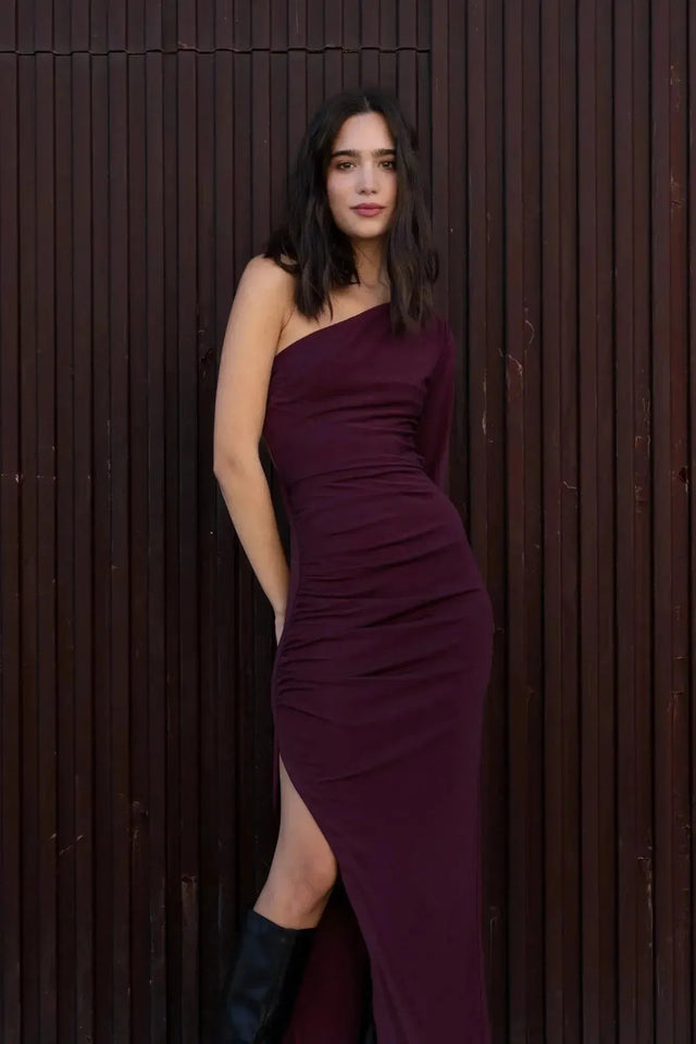 Femme posant dans la robe asymétrique une manche bordeaux, soulignant la coupe flatteuse et l'élégance.