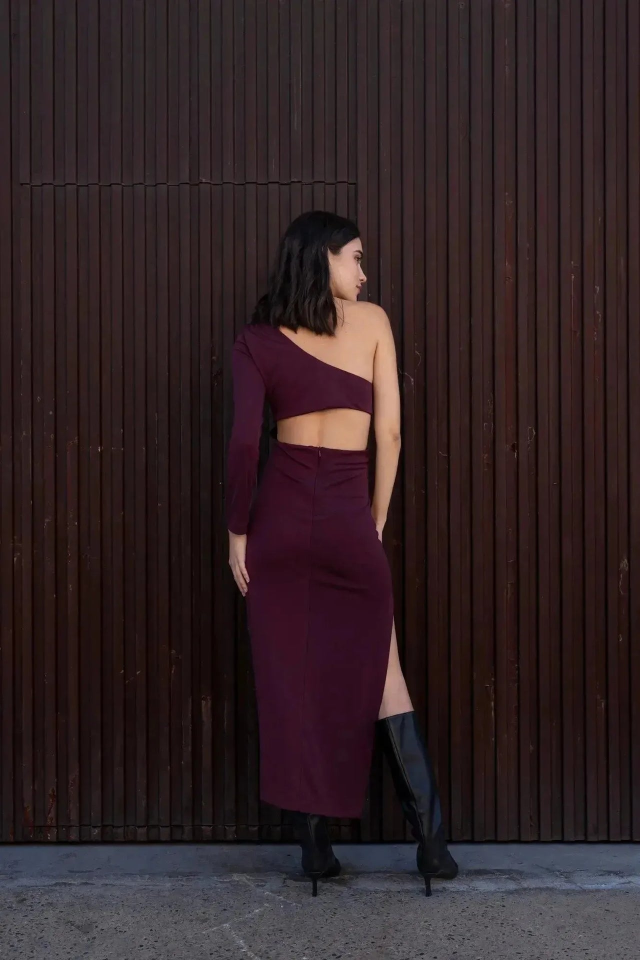 Vue arrière du modèle en robe asymétrique une manche bordeaux, montrant le design distinctif et élégant.