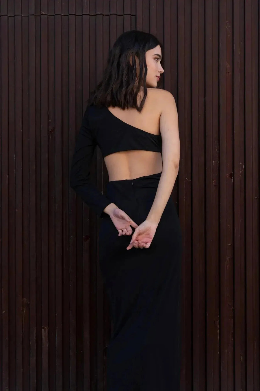 Vue de côté de la robe asymétrique une manche noire sur le modèle, montrant la coupe flatteuse et moderne.