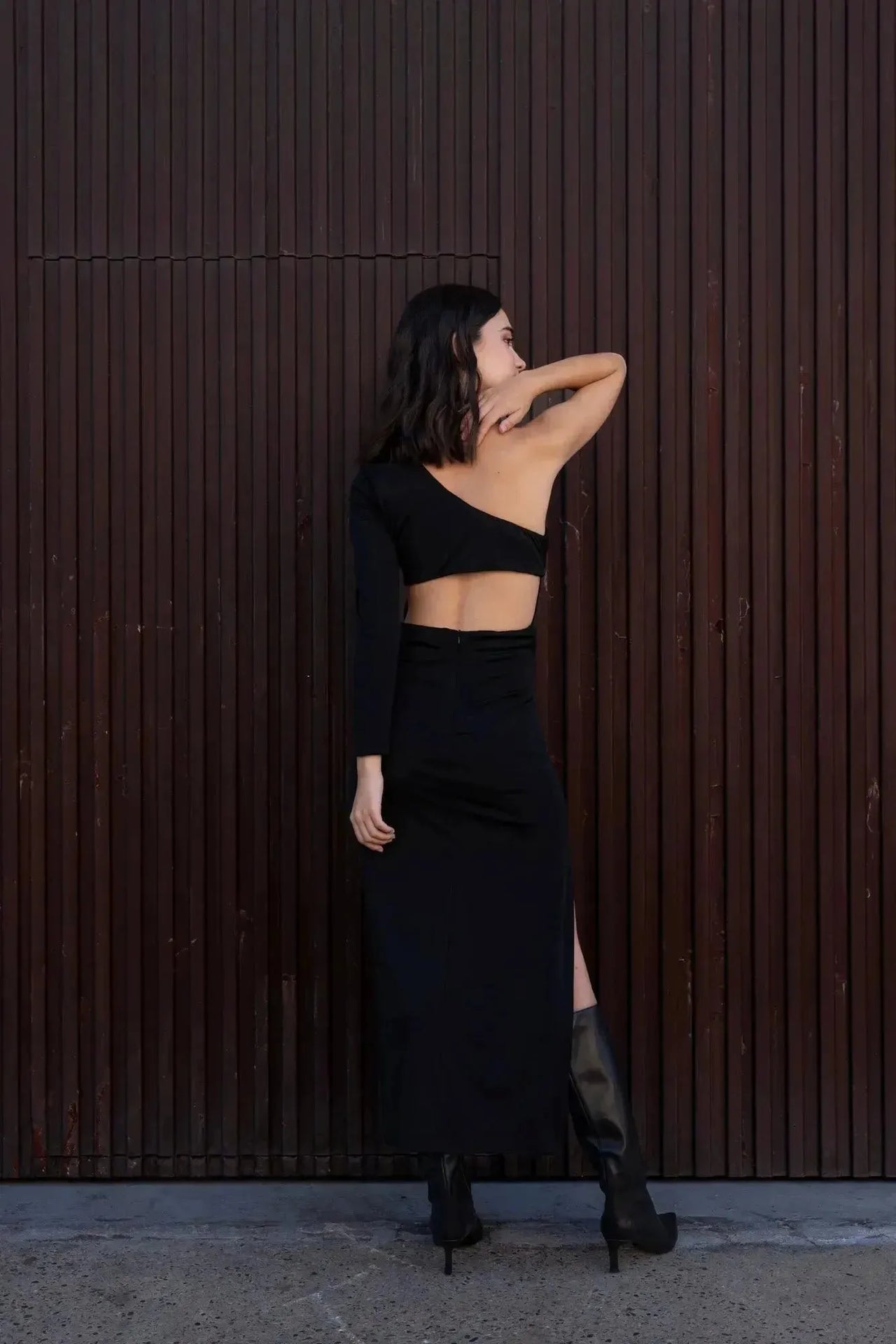 Femme en position de pose relaxée, mettant en avant la robe asymétrique une manche noire, parfaite pour les événements élégants.