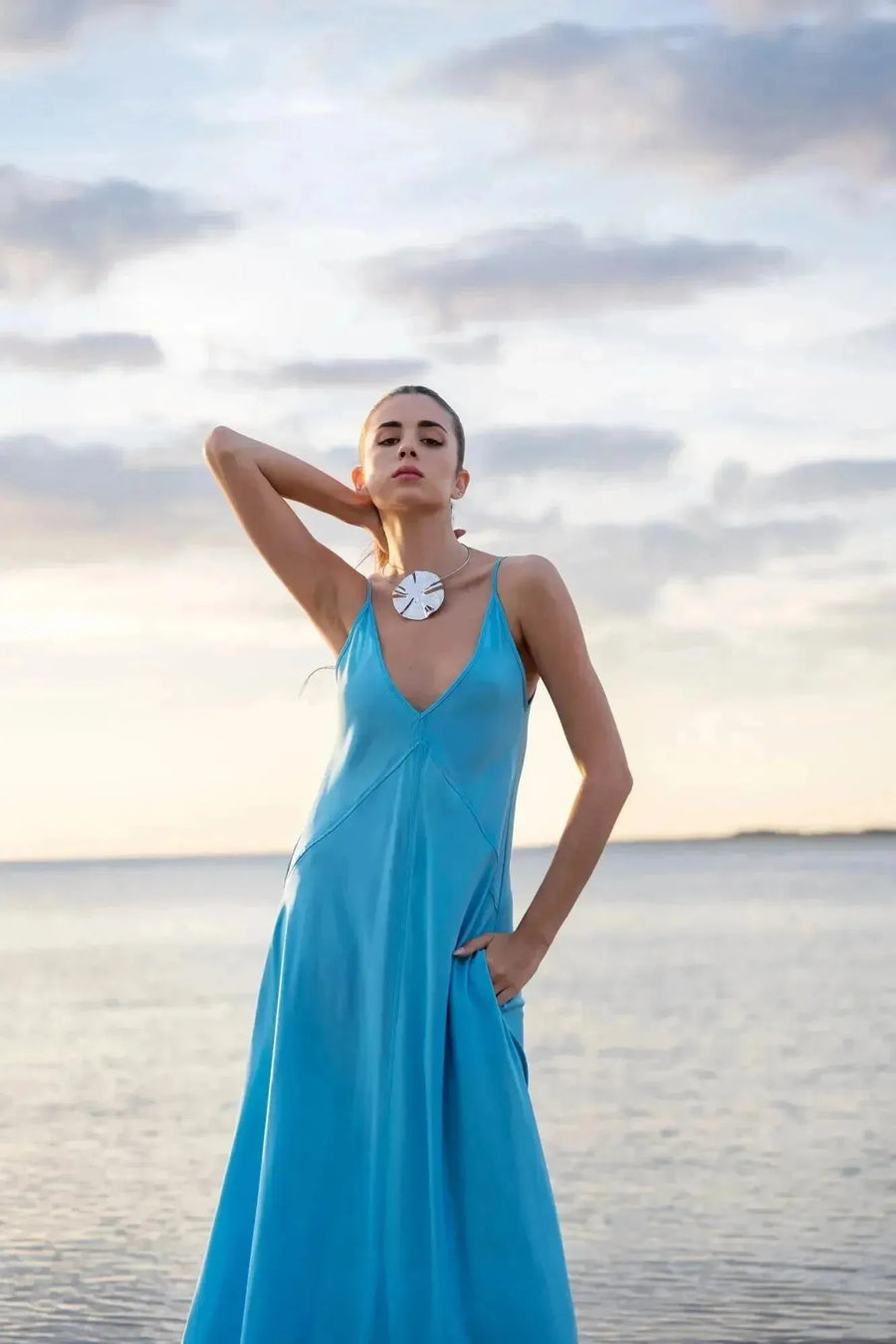 Femme posant élégamment sur la plage dans une robe longue bretelles fines, fluide et légère, idéale pour les soirées d'été.