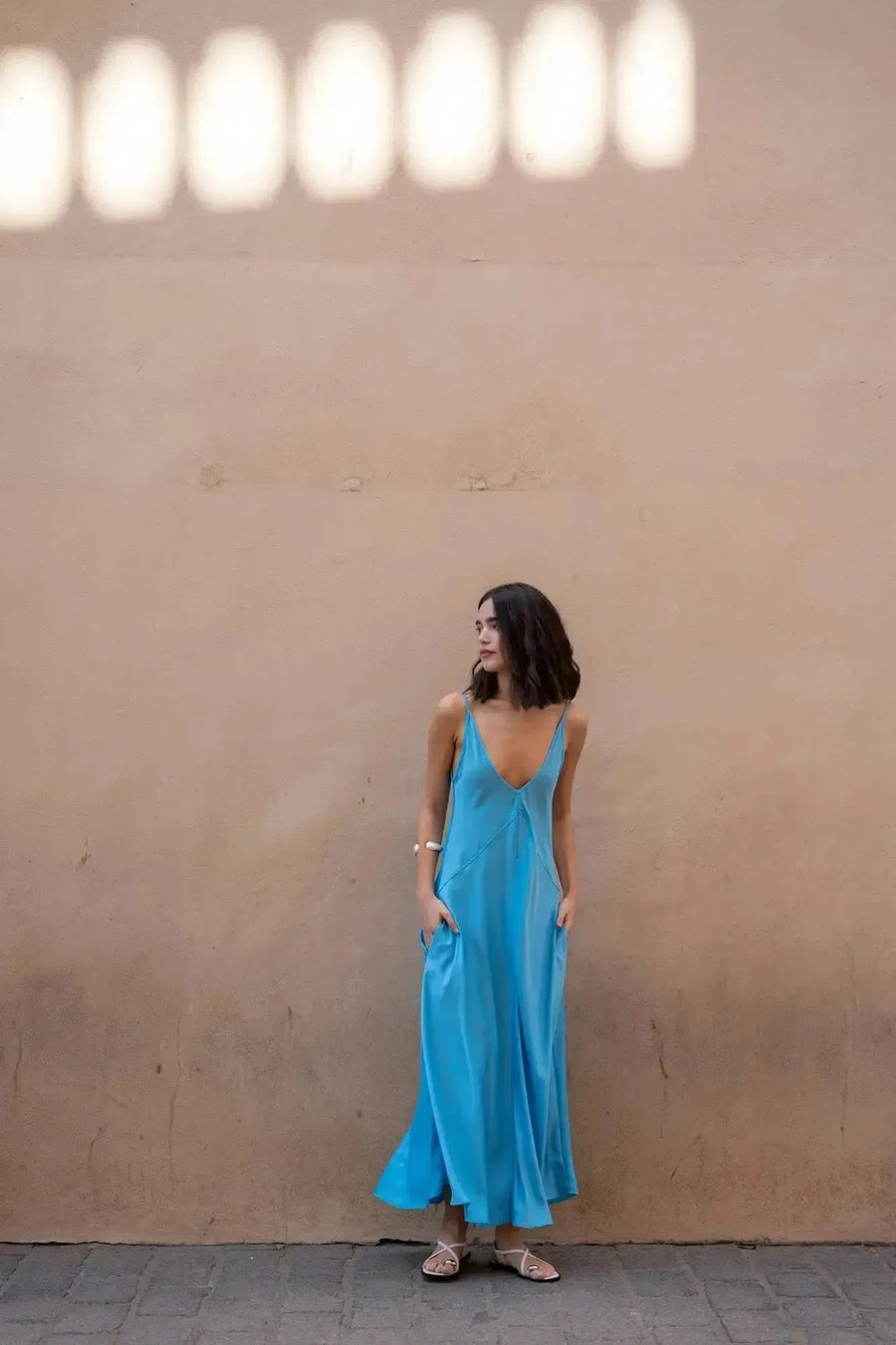 Modèle portant la robe longue bretelles fines fluide midi pour été, avec un fond de mur beige. Élégante et confortable, parfaite pour l'été.