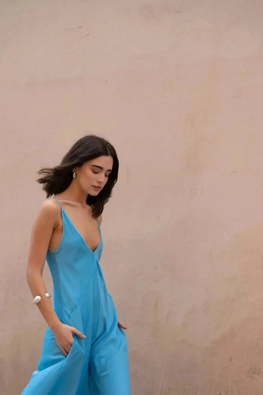 Femme marchant avec grâce dans la robe longue bretelles fines, couleur bleu, sur un fond beige, montrant le style décontracté et élégant.