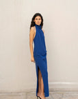 Model dans une robe longue dos nu Sapiato bleue, se tenant de profil avec une fente élégante, incarnation parfaite d'un style chic.