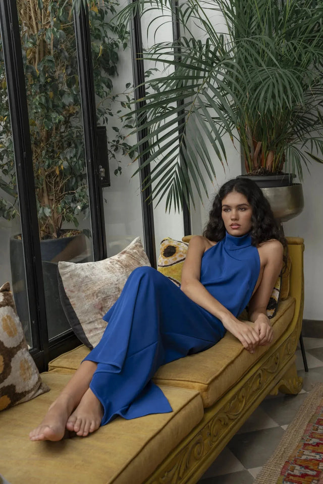 Model relaxant dans une robe longue dos nu Sapiato, assise sur un canapé, respirant l'élégance et le confort.